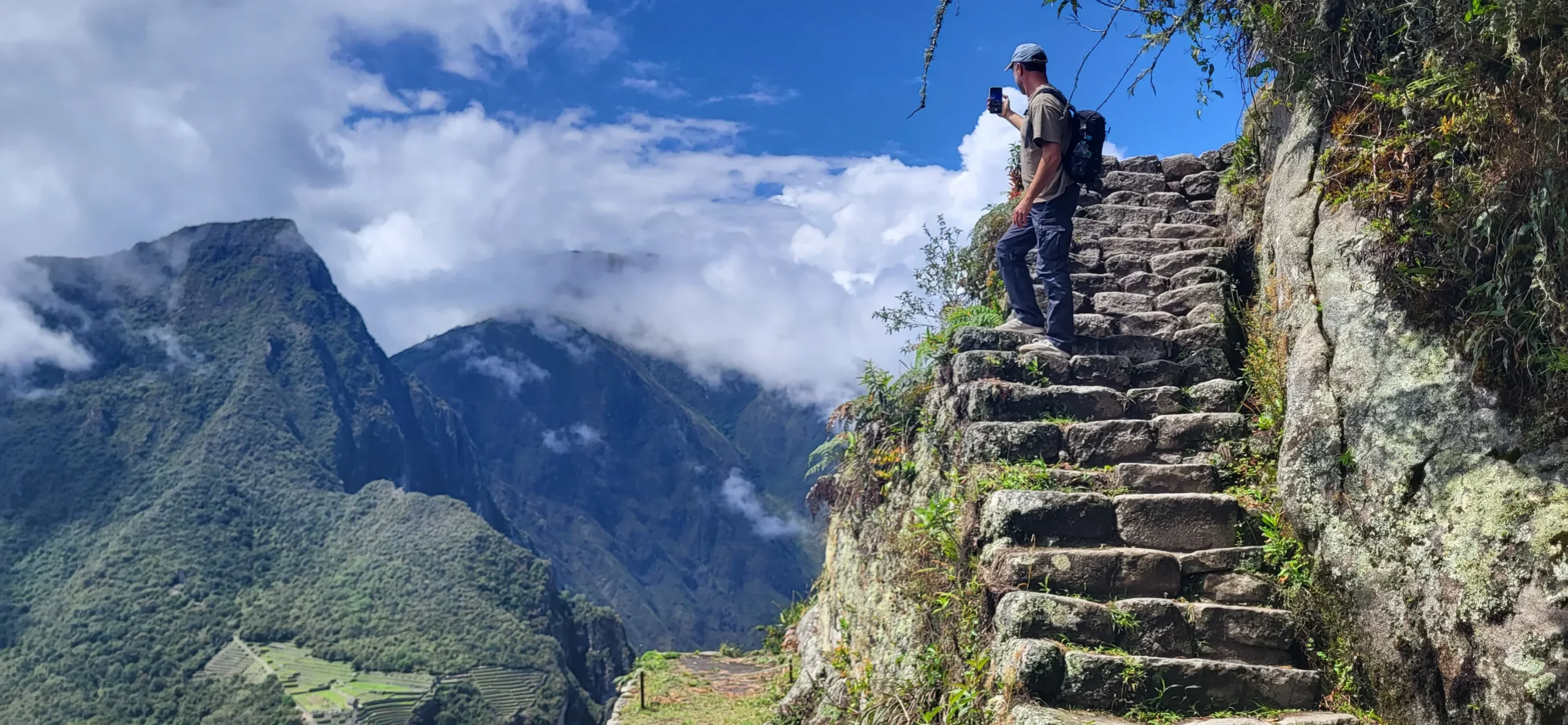 Traveler walking down ancient Inca stone steps with Andean mountains and clouds in the background, Peru