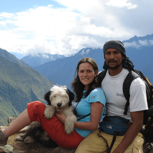 Two Santu team members and a dog resting on an Andean mountainside above a green valley, Peru
